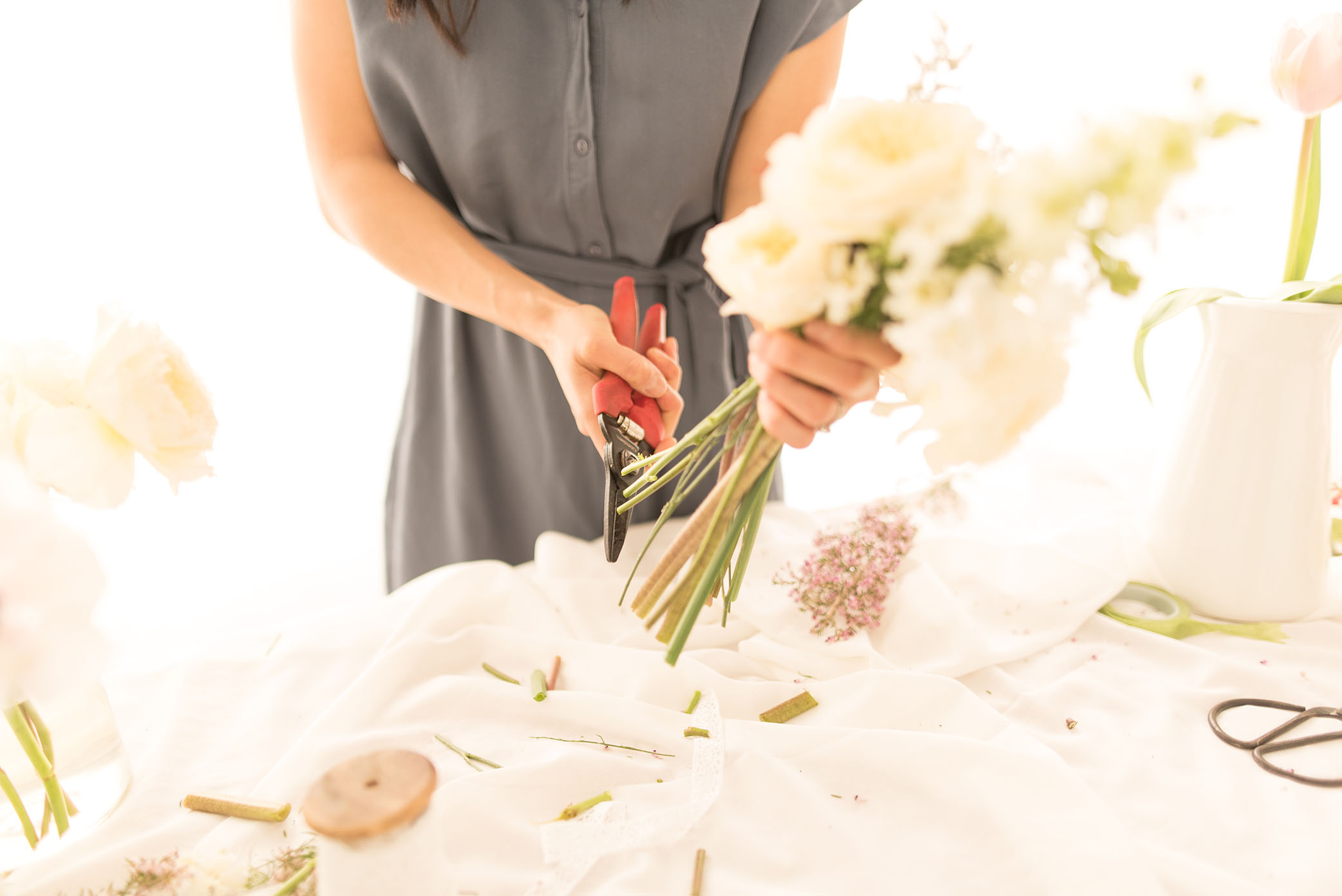 A woman trims the stems of flowers. 