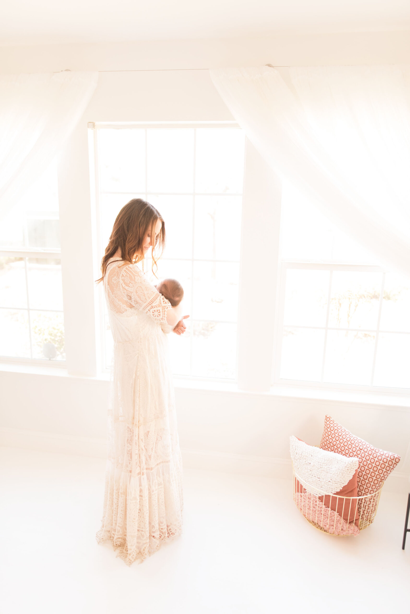 A mother stands by a window with tons of light holding her newborn. 