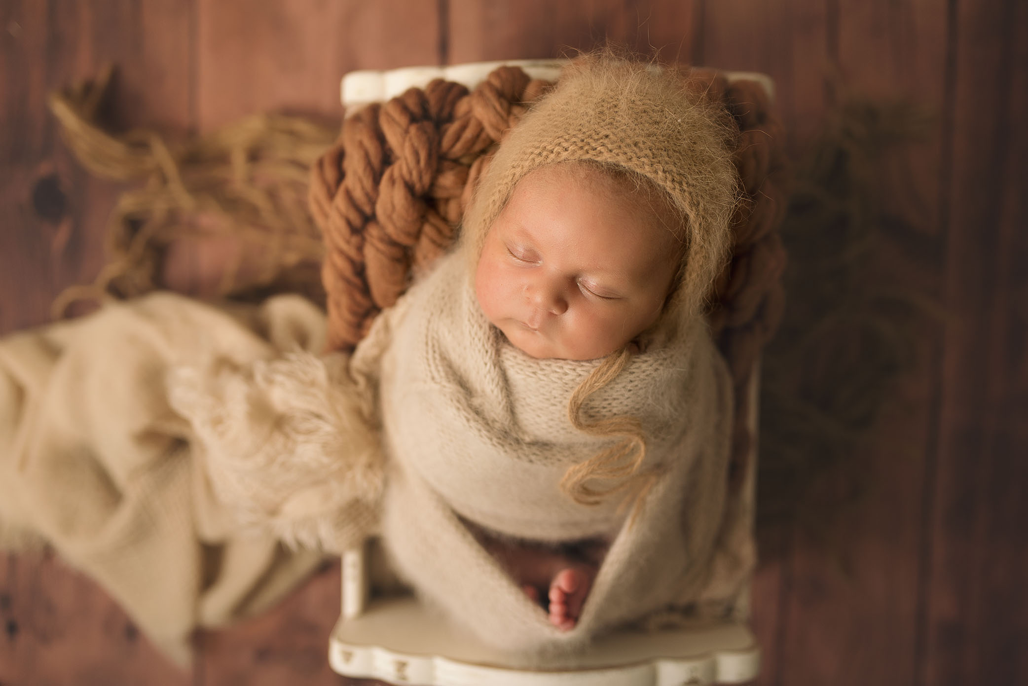 A newborn baby girl sleeps on top of a textured brown blanket. 