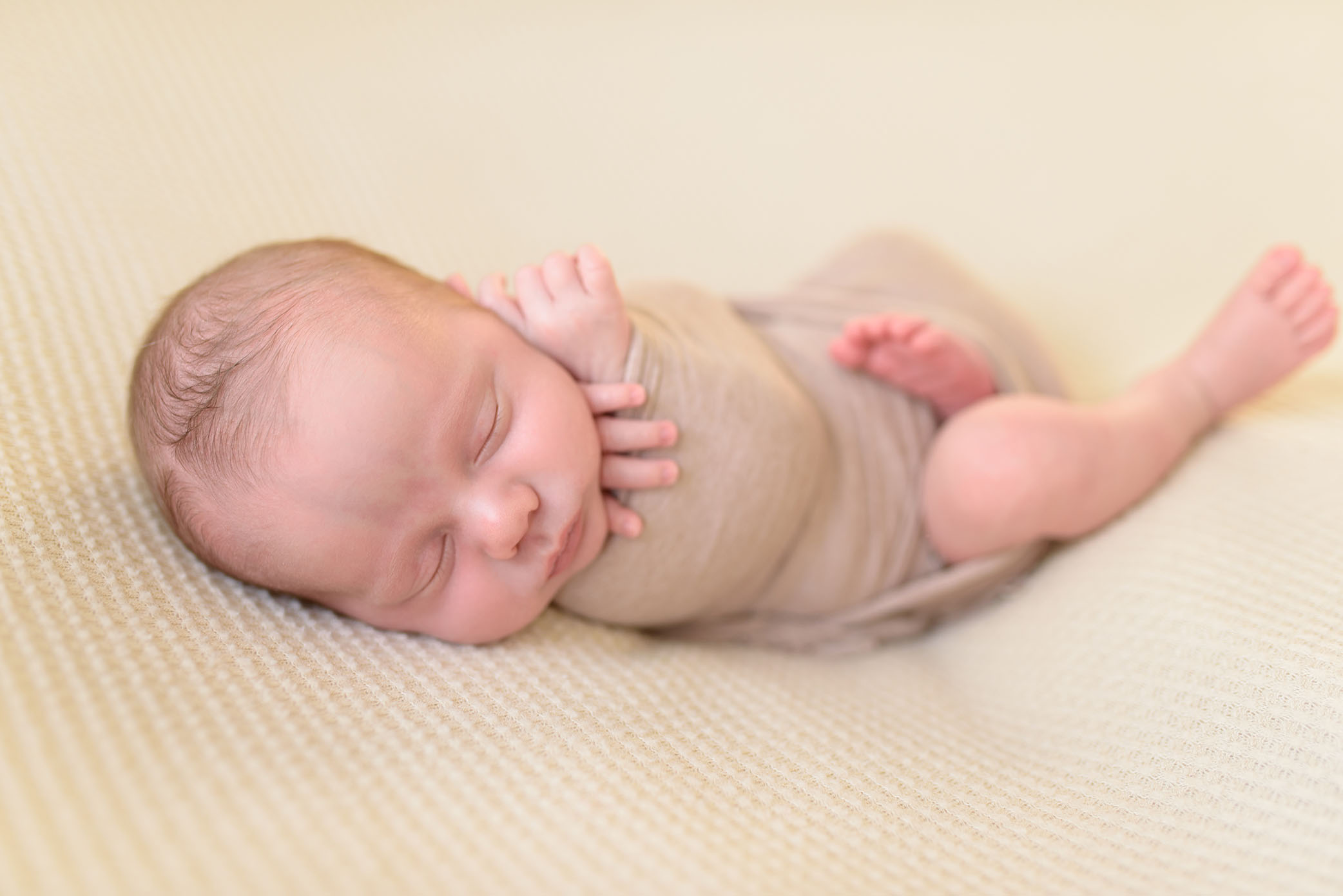 Newborn wrapped in beige swaddle on beanbag captured by Sweet Beginnings Photography by Stephanie