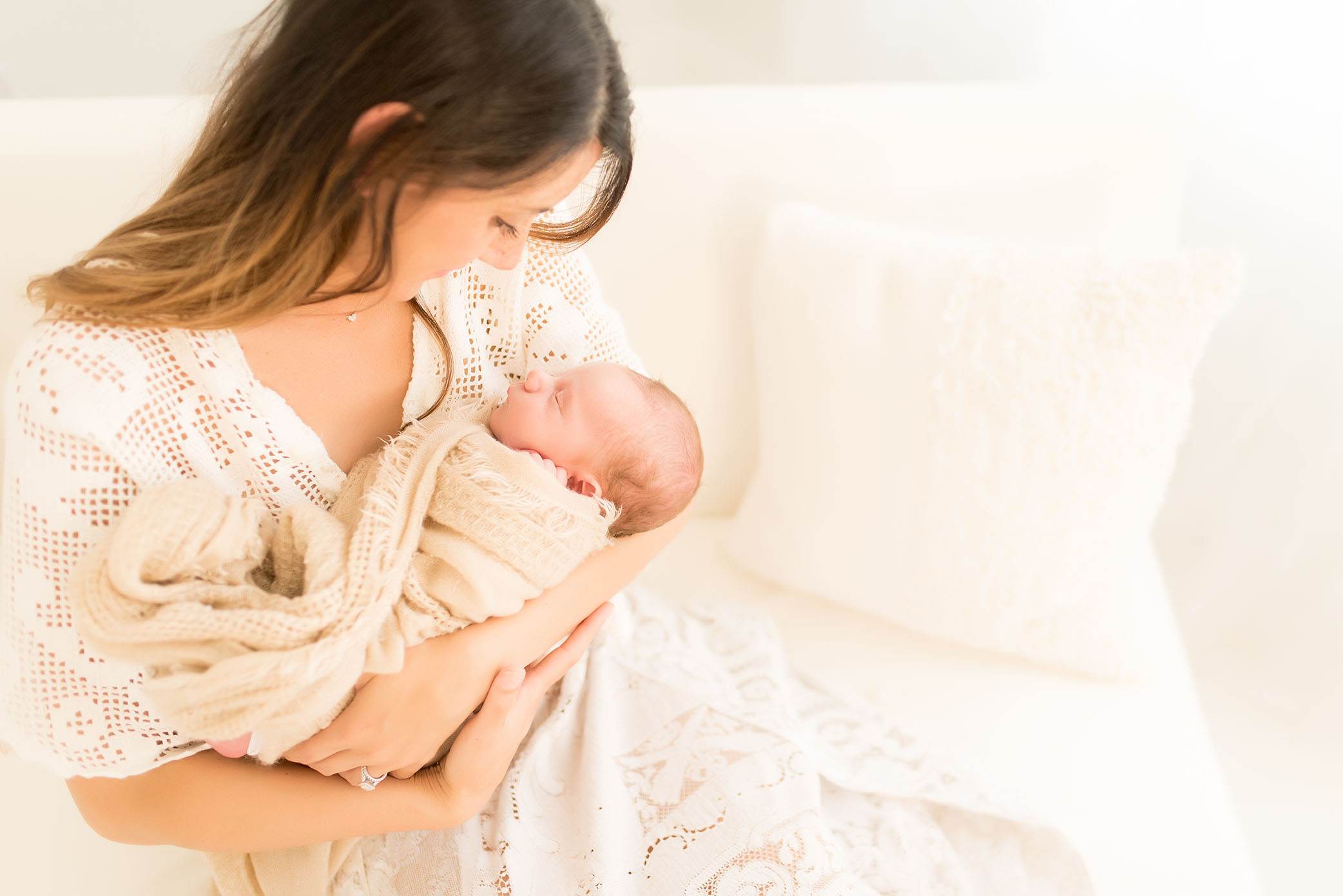 Mother holds her are baby wearing all white captured by Sweet Beginnings Photography by Stephanie