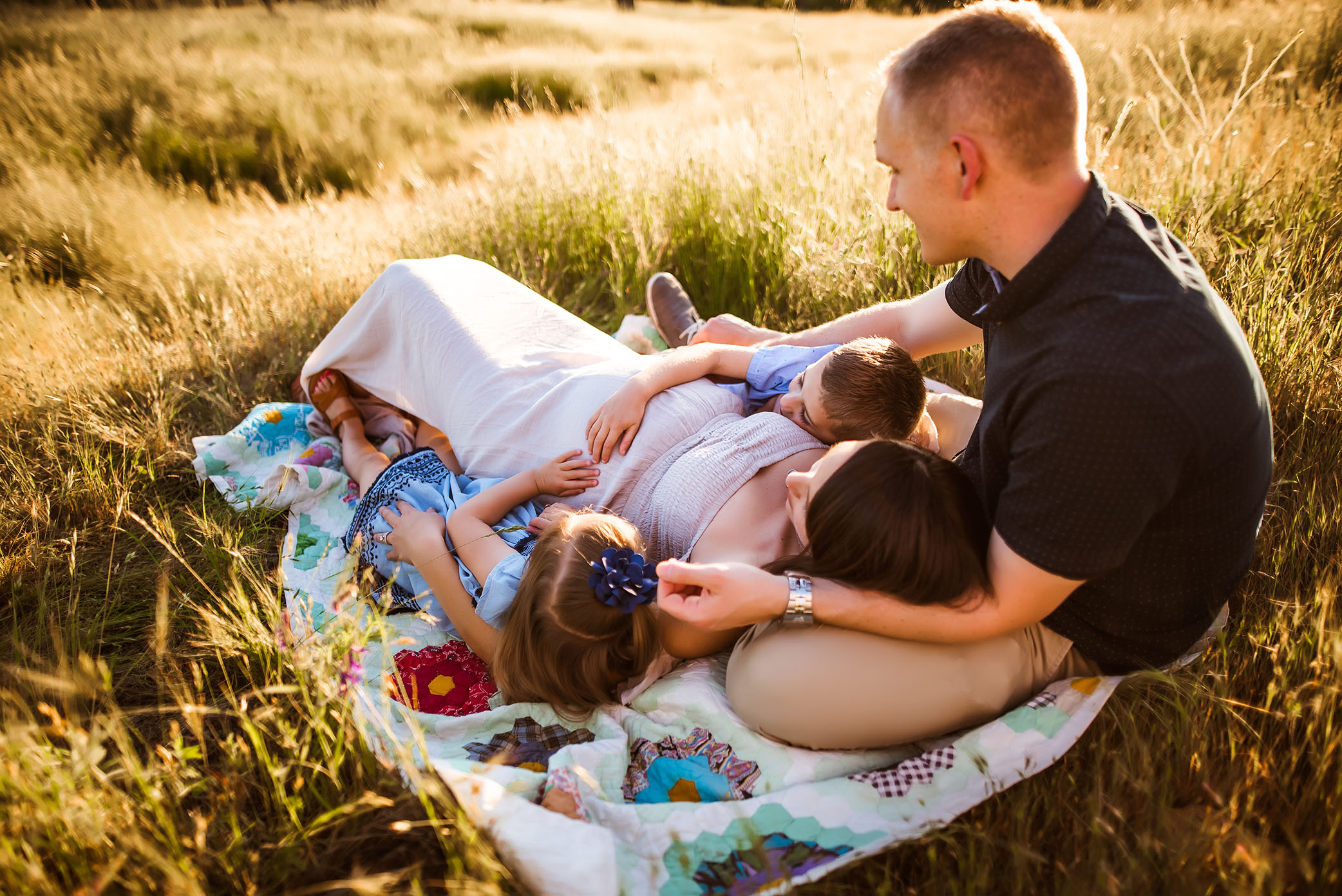Family lays on a blanket in the sun captured by Sweet Beginnings Photography by Stephanie