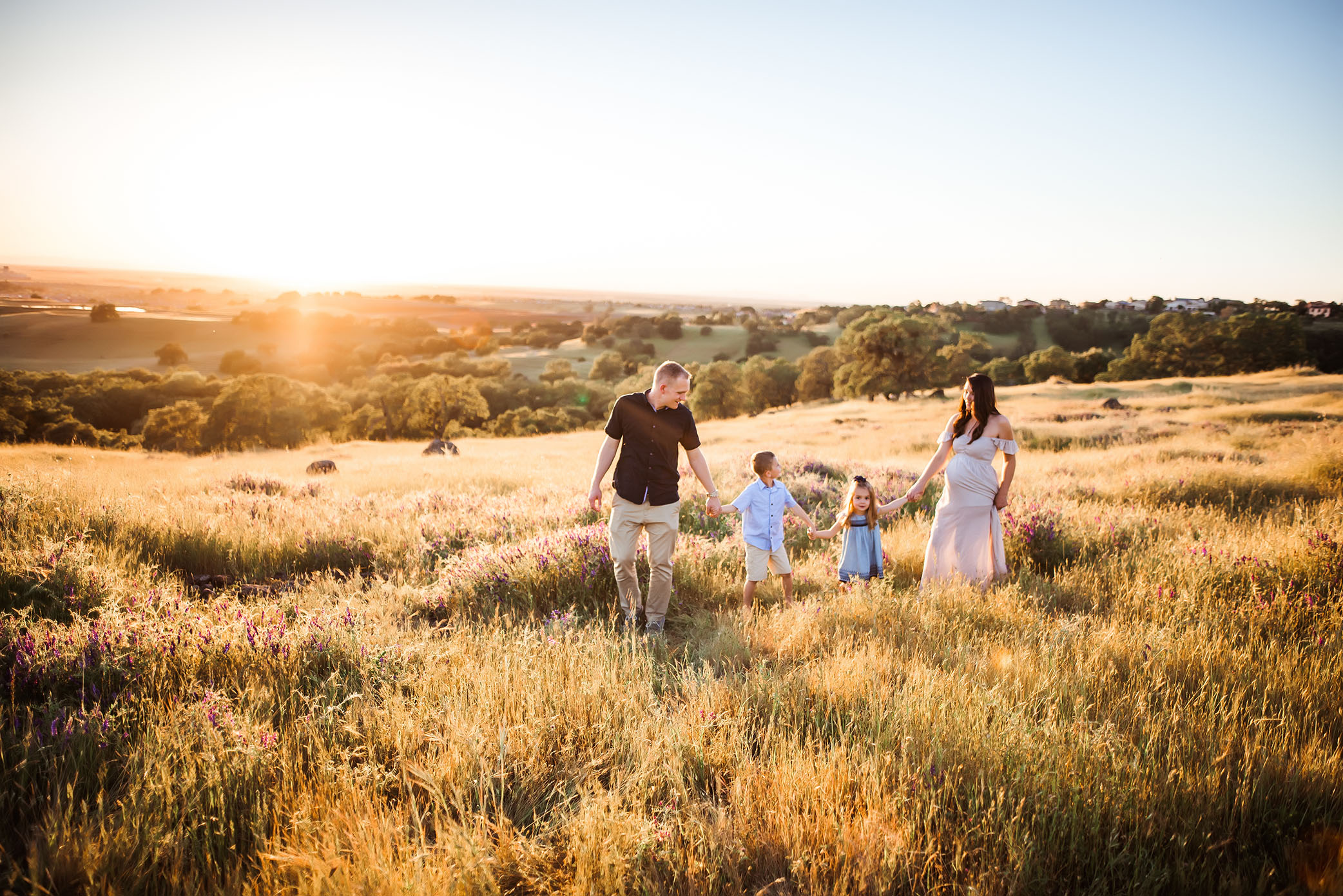A growing family walks together in the sunshine captured by Sweet Beginnings Photography by Stephanie