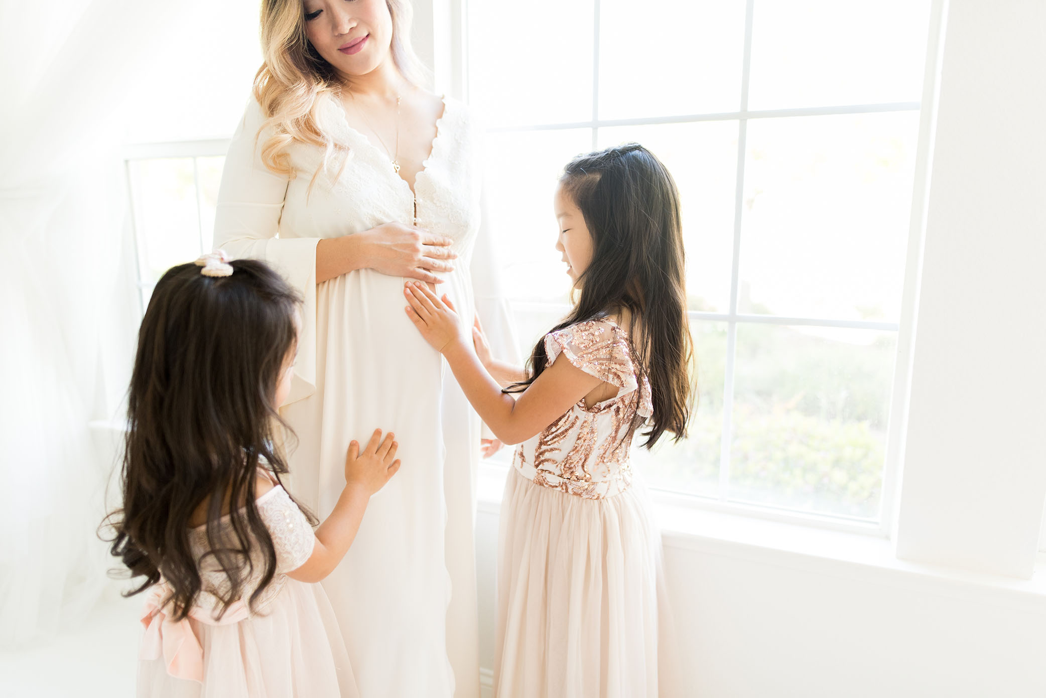 Daughter touches her moms pregnant belly in studio captured by Sweet Beginnings Photography by Stephanie