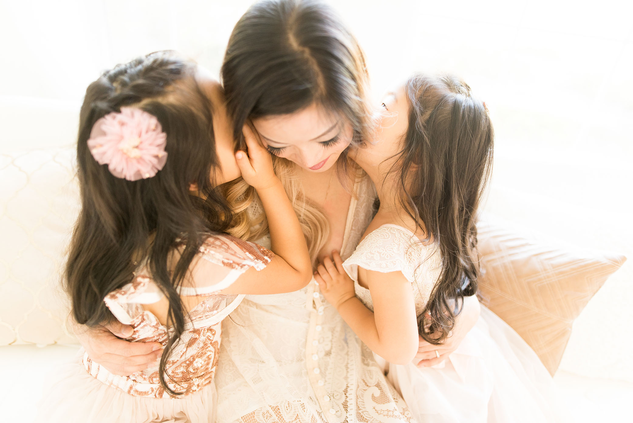 A mom listens to whispers in her ear by two daughters captured by Sweet Beginnings Photography by Stephanie