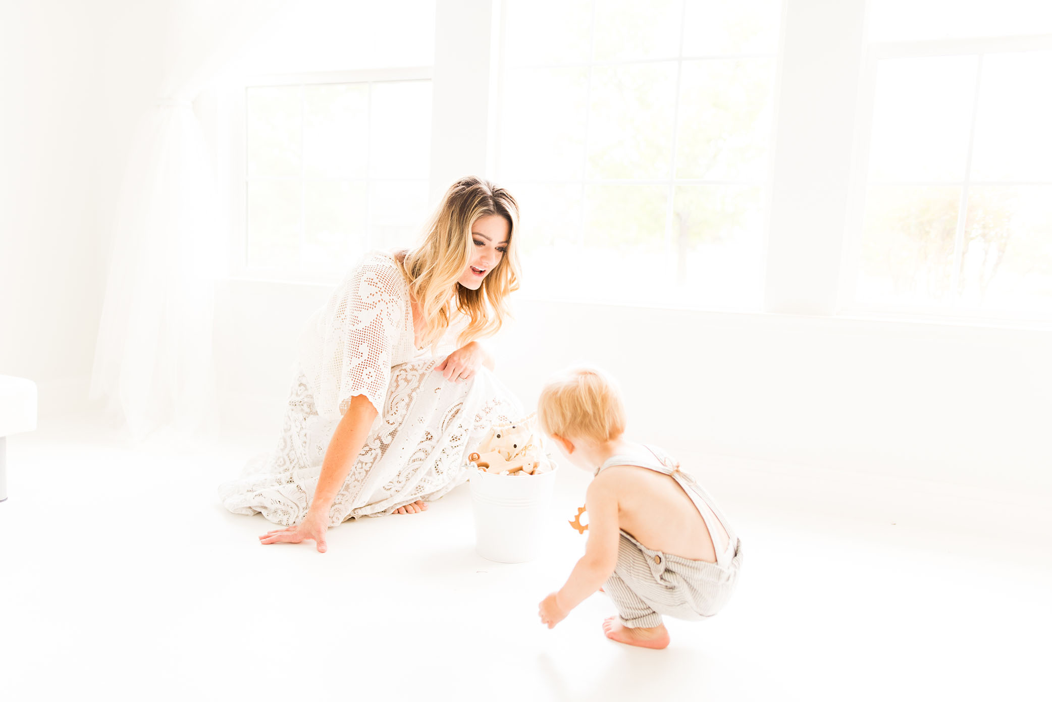 Mom plays with son on the floor dressed in white captured by Sweet Beginnings Photography by Stephanie