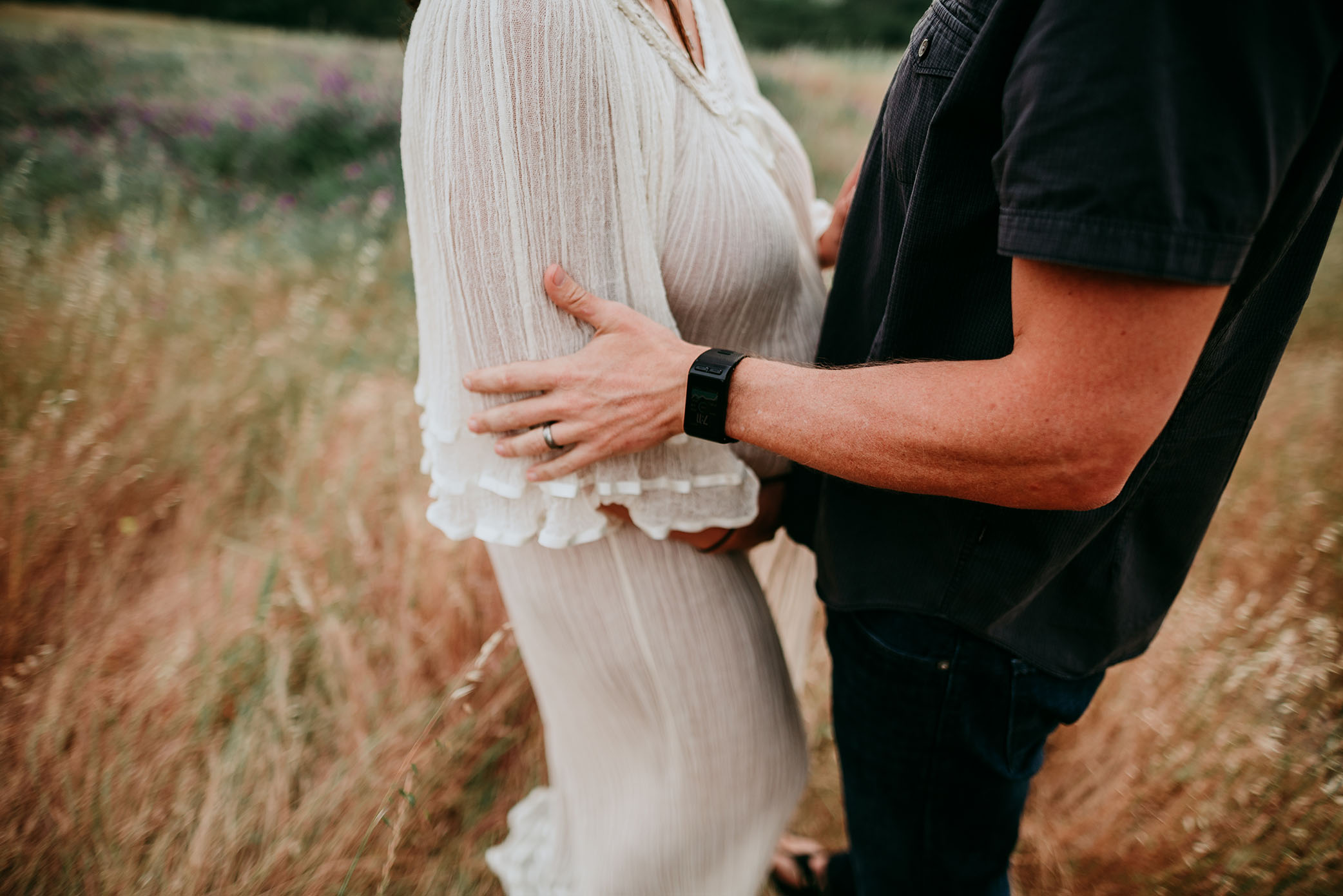 Husband holds wife arm as they embrace their upcoming baby's arrival captured by Sweet Beginnings Photography by Stephanie