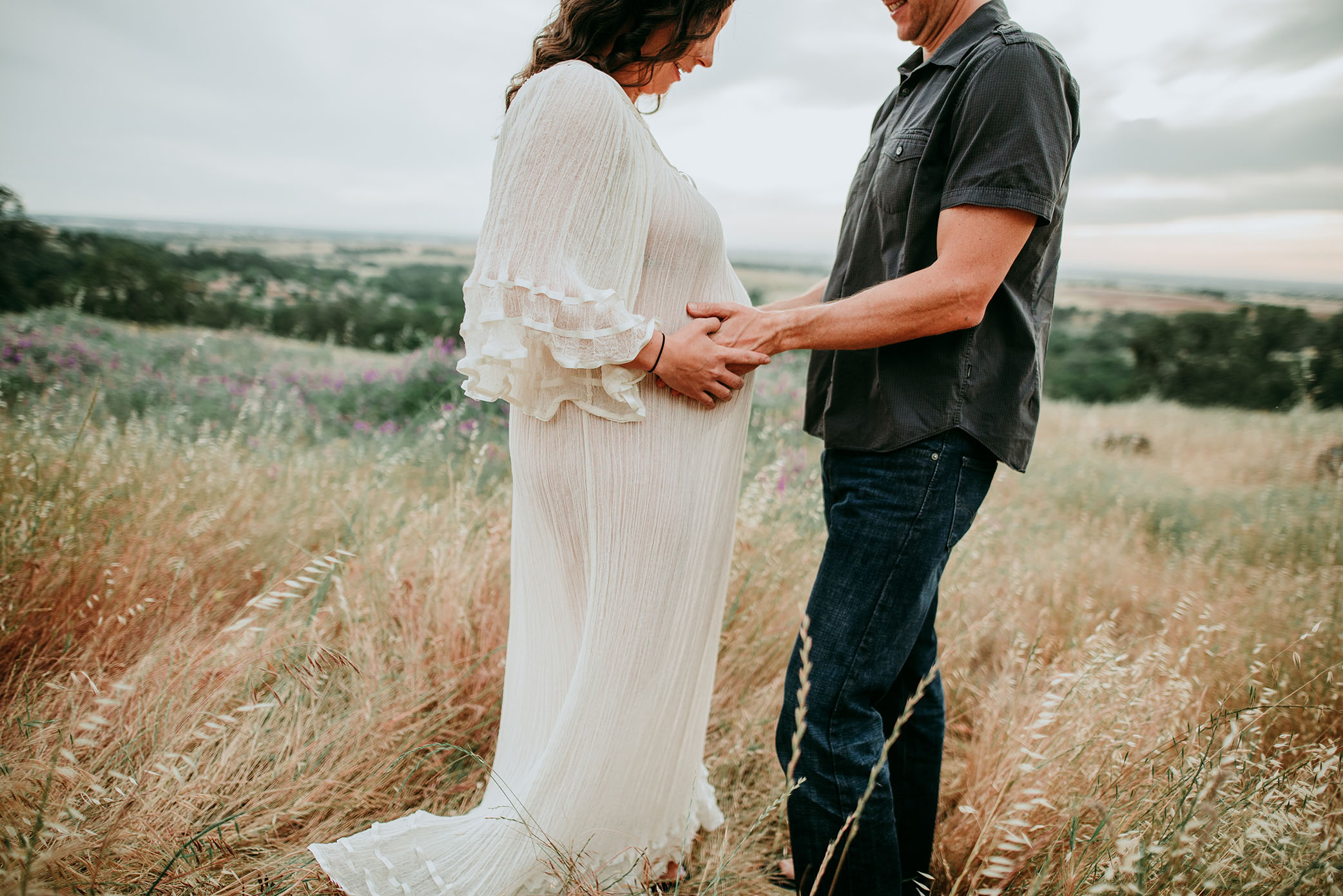 Husband looks at wife's pregnant belly on hill captured by Sweet Beginnings Photography by Stephanie