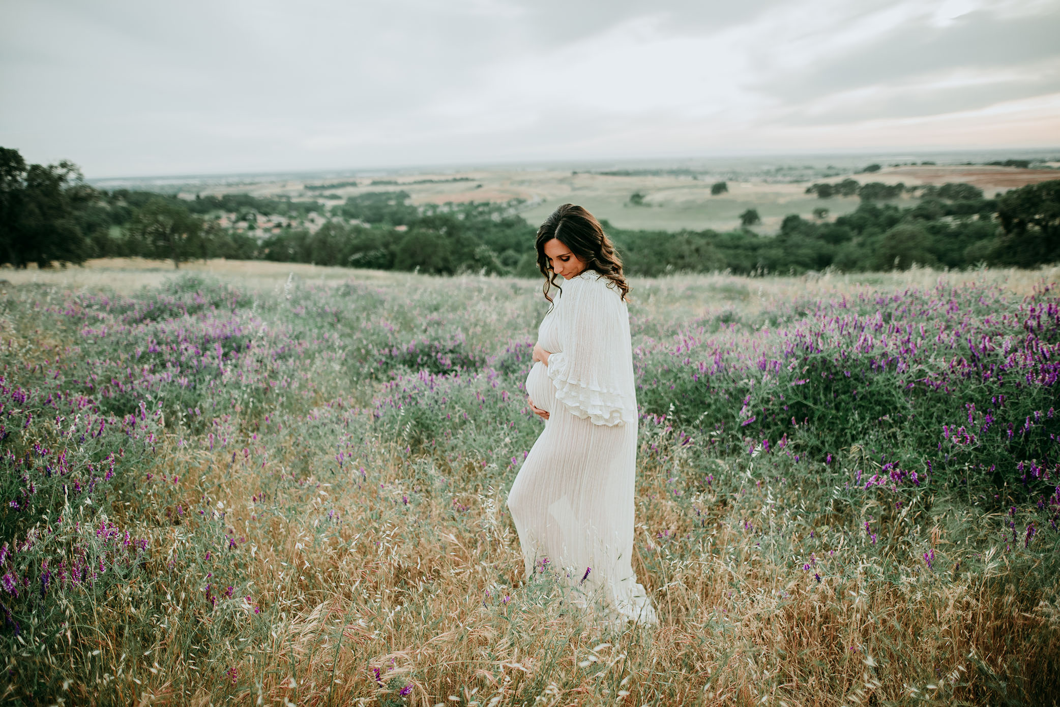 Pregnant woman holds belly on beautiful hill captured by Sweet Beginnings Photography by Stephanie