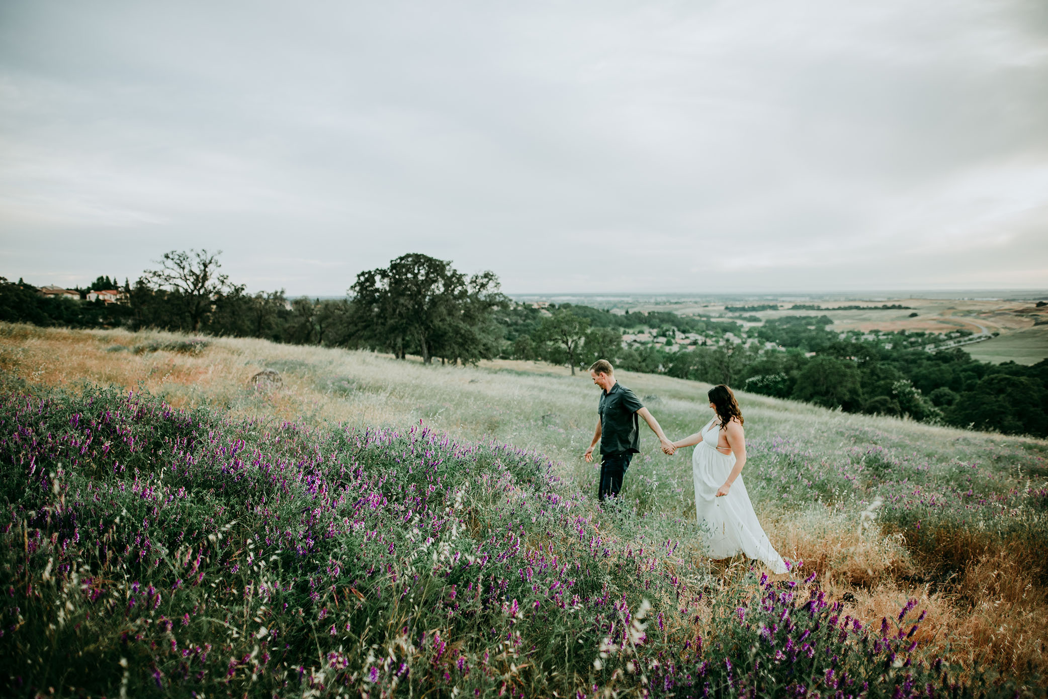 Maternity photo of couple walking though wildflowers captured by Sweet Beginnings Photography by Stephanie
