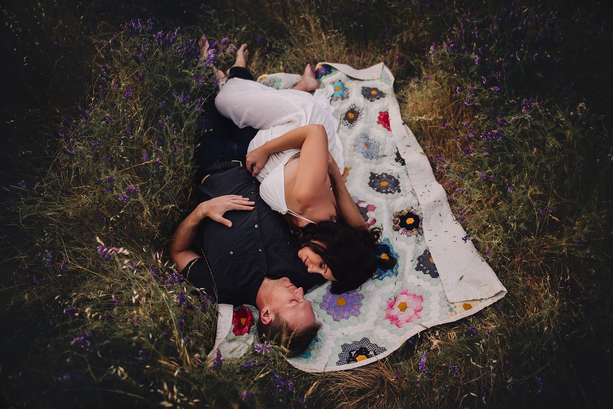 Husband and pregnant wife lay on a blanket in wildflowers captured by Sweet Beginnings Photography by Stephanie