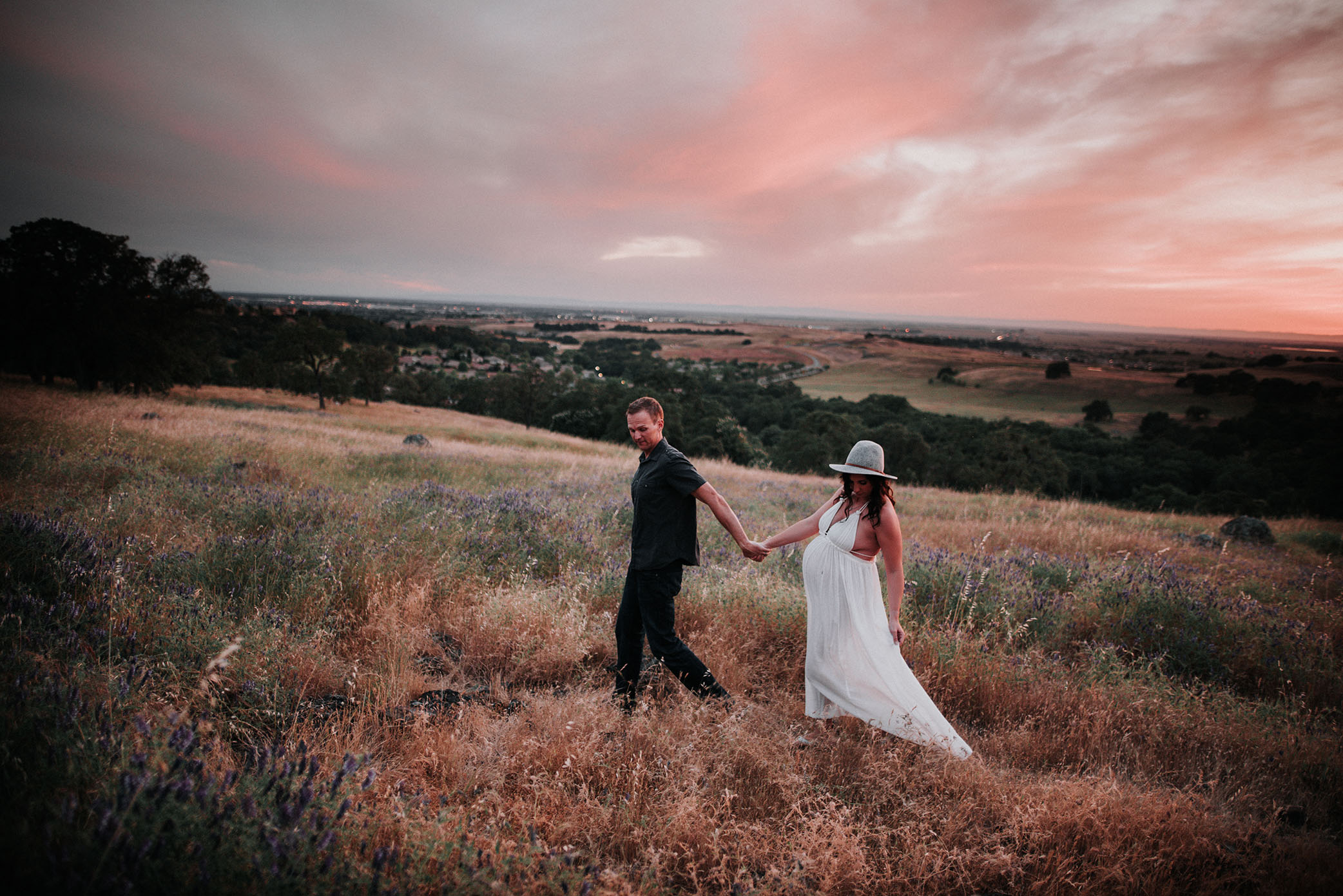 Expectant mom and dad walk on hillside captured by Sweet Beginnings Photography by Stephanie