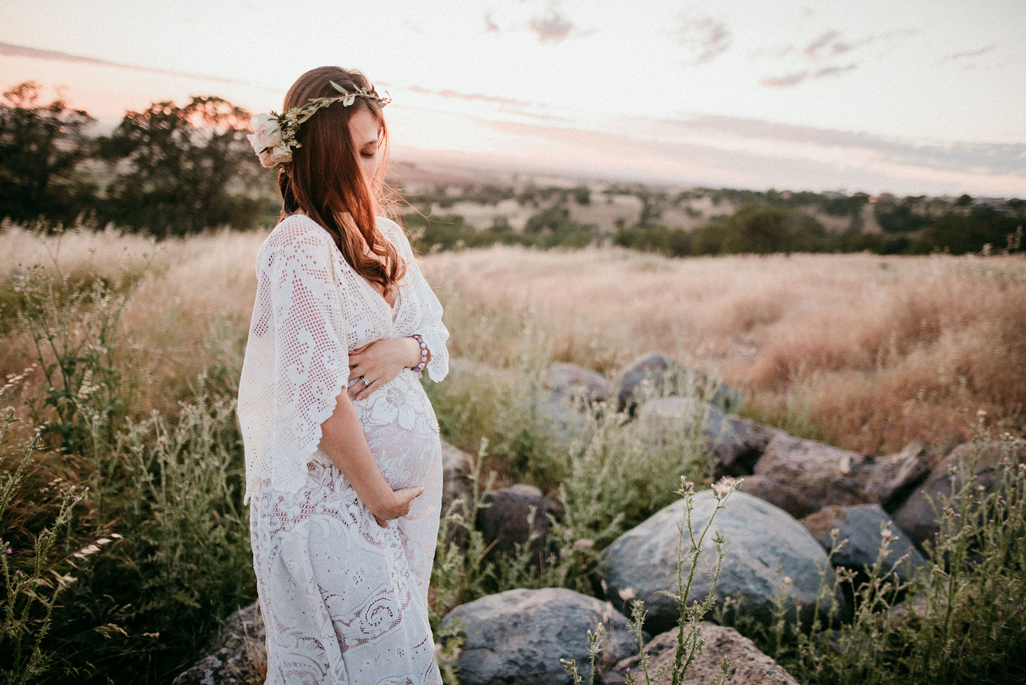 Pregnant mom look down at her belly in white lace dress captured by Sweet Beginnings Photography by Stephanie