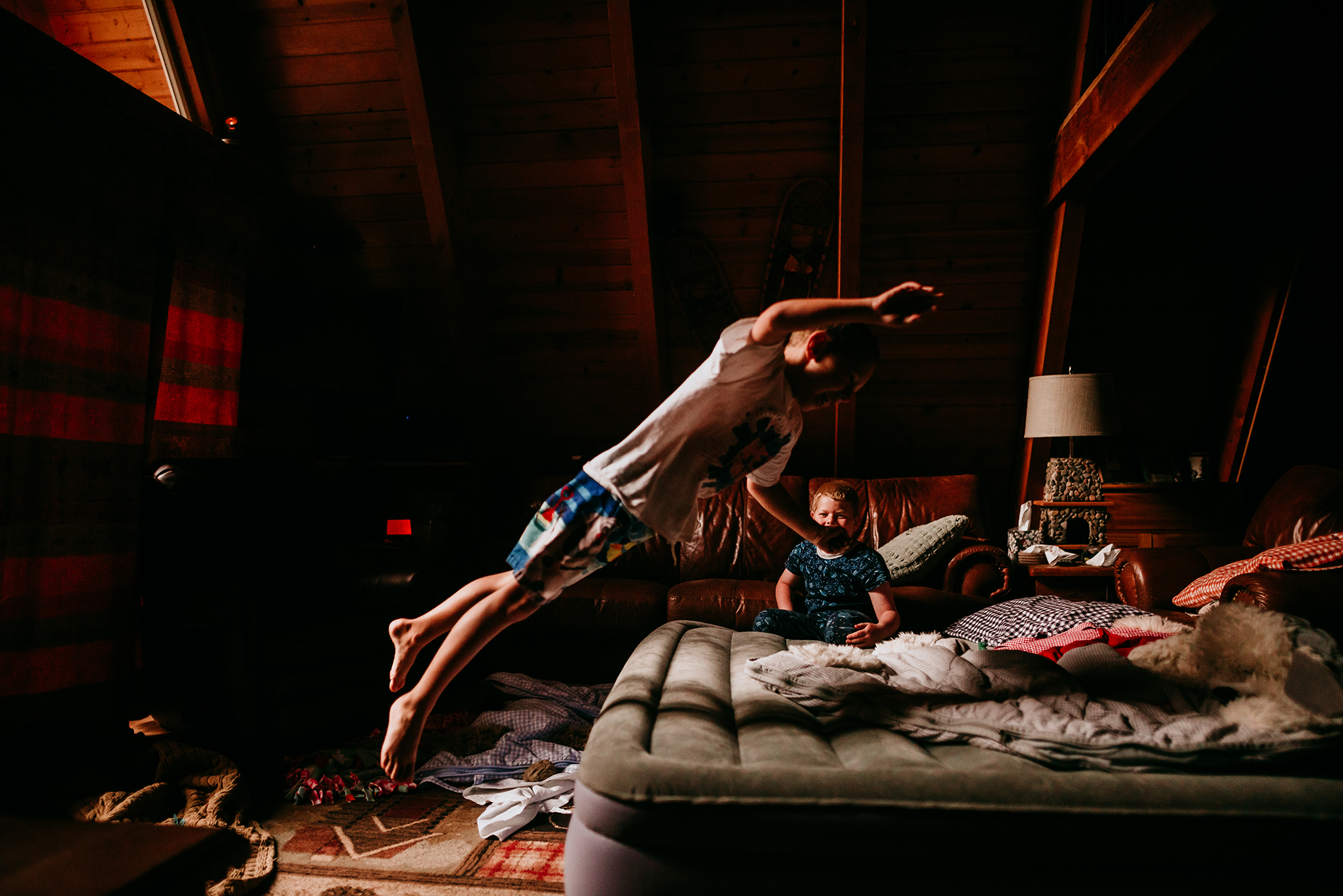 Little boy leaps onto air mattress in cabin