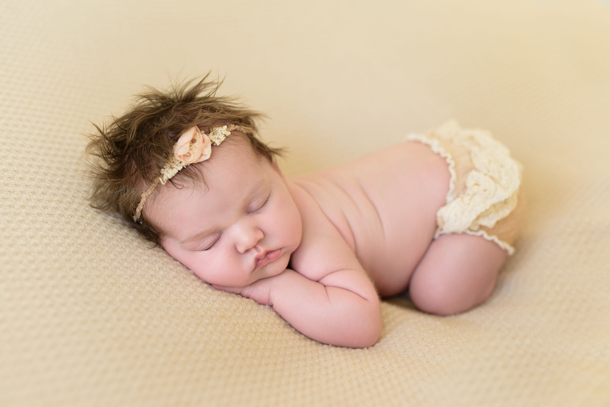 Newborn baby posed on her tummy in beige