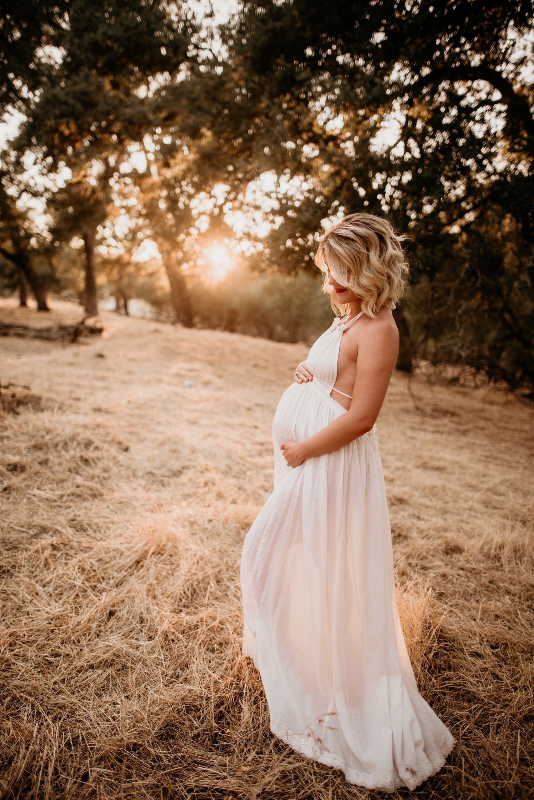 Mama to be holds her belly in white dress