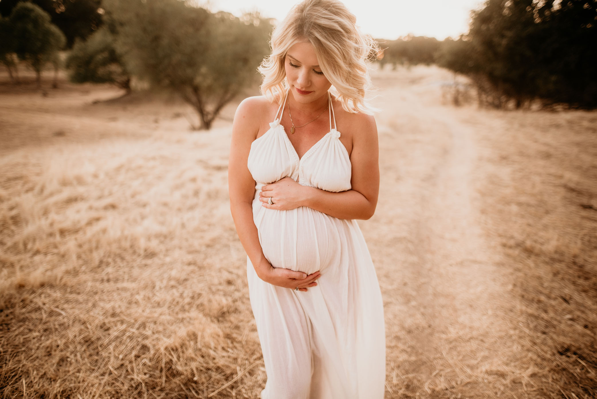 Mother to be holds her bump while looking down in white dress