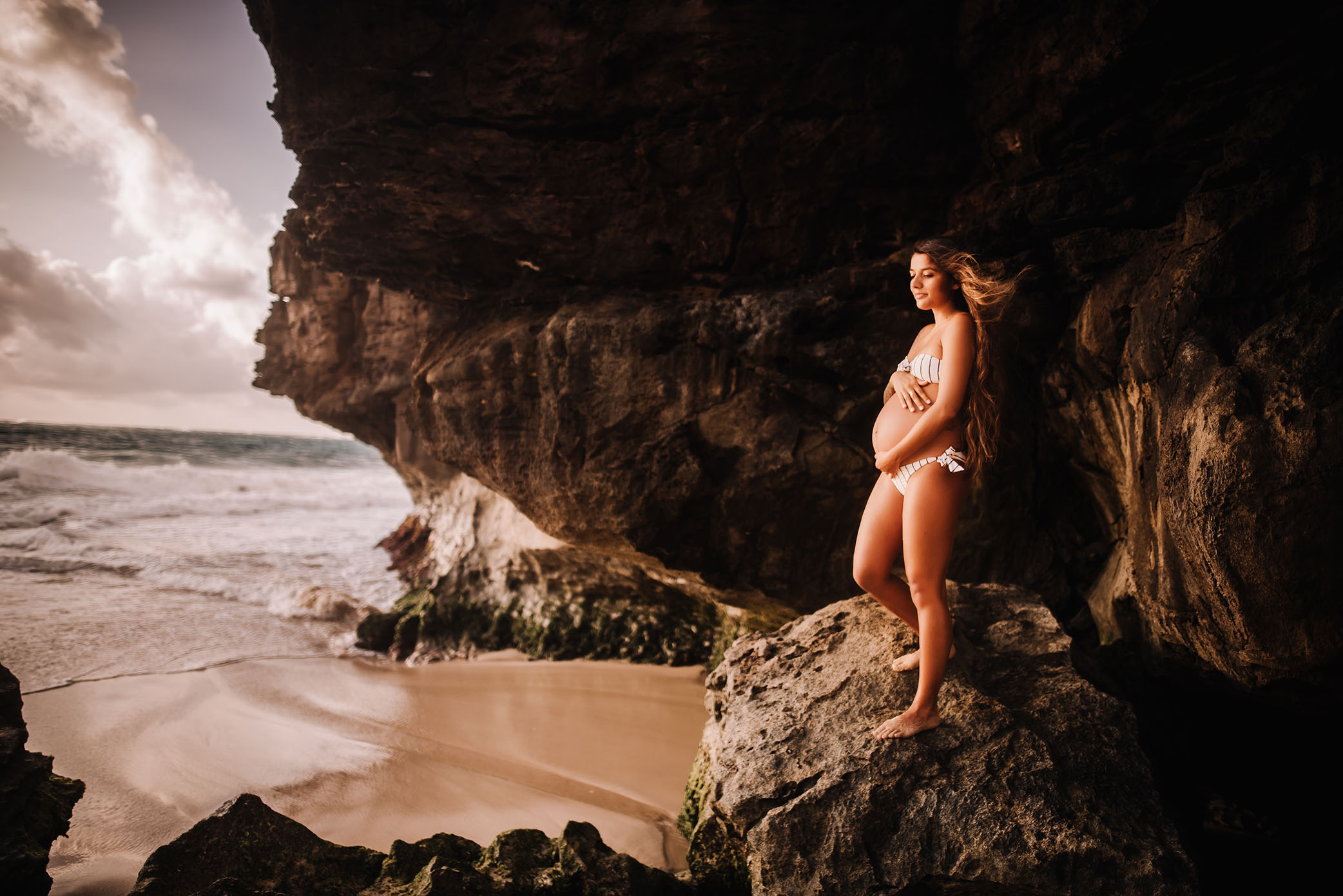 Pregnant mama holds her belly looking at ocean
