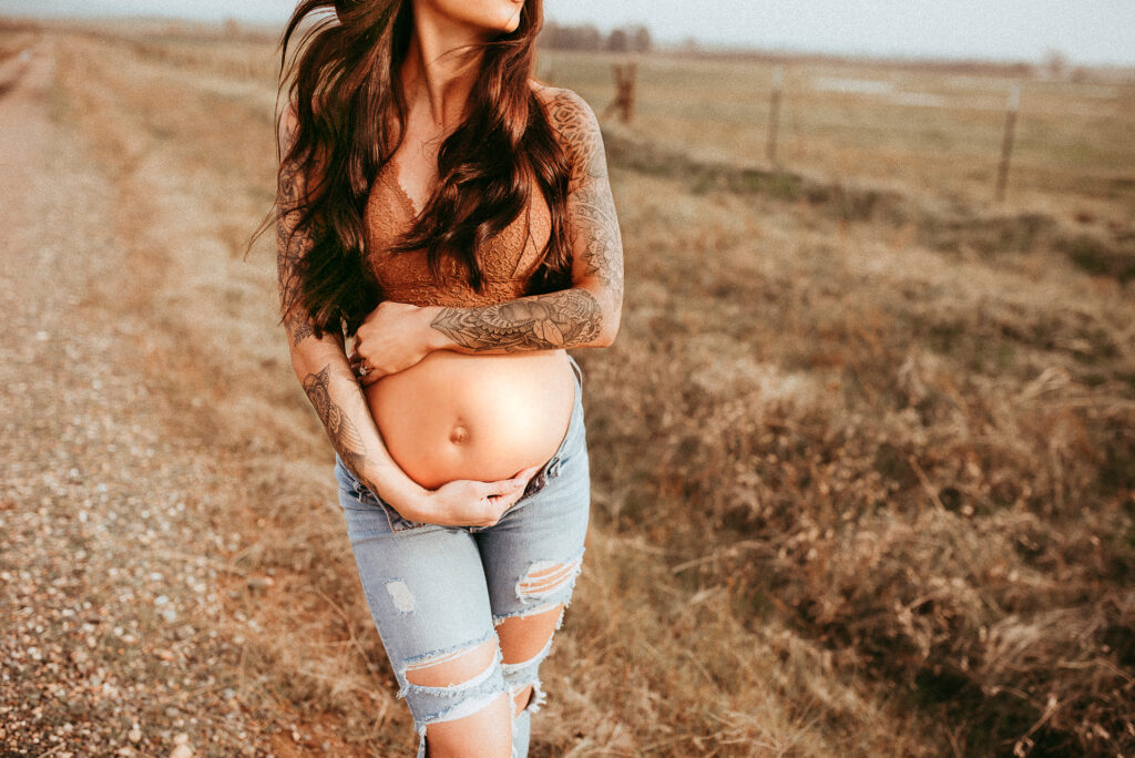 Pregnant mama holds belly while looking over her shoulder, hair blowing in wind